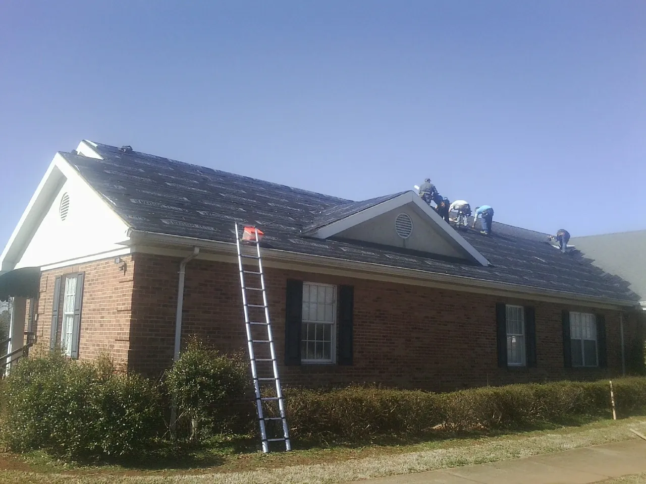Crew tearing shingles off a brick ranch roof with a ladder set — Metal Roof Repair work by our crew in Duncanville