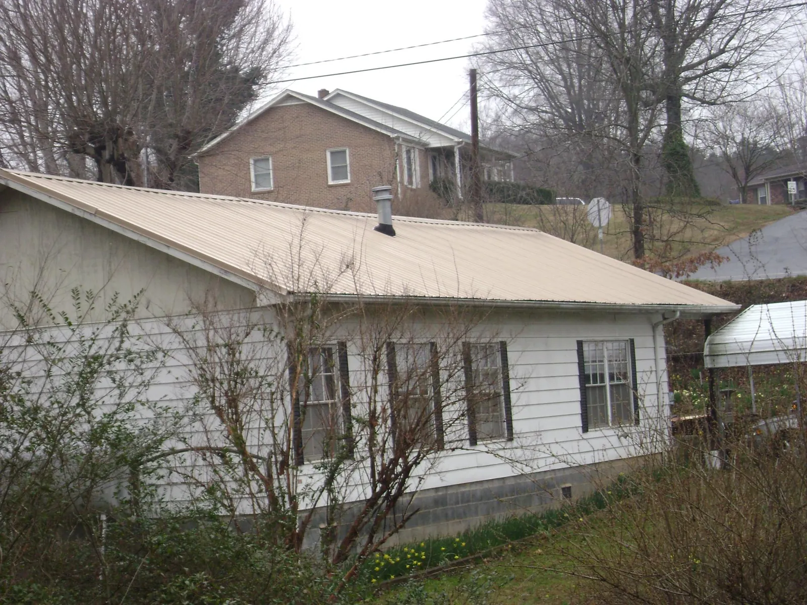 Tan metal roof on a white sided house set into a hillside — Commercial Roofing by Roofing Brothers in Duncanville