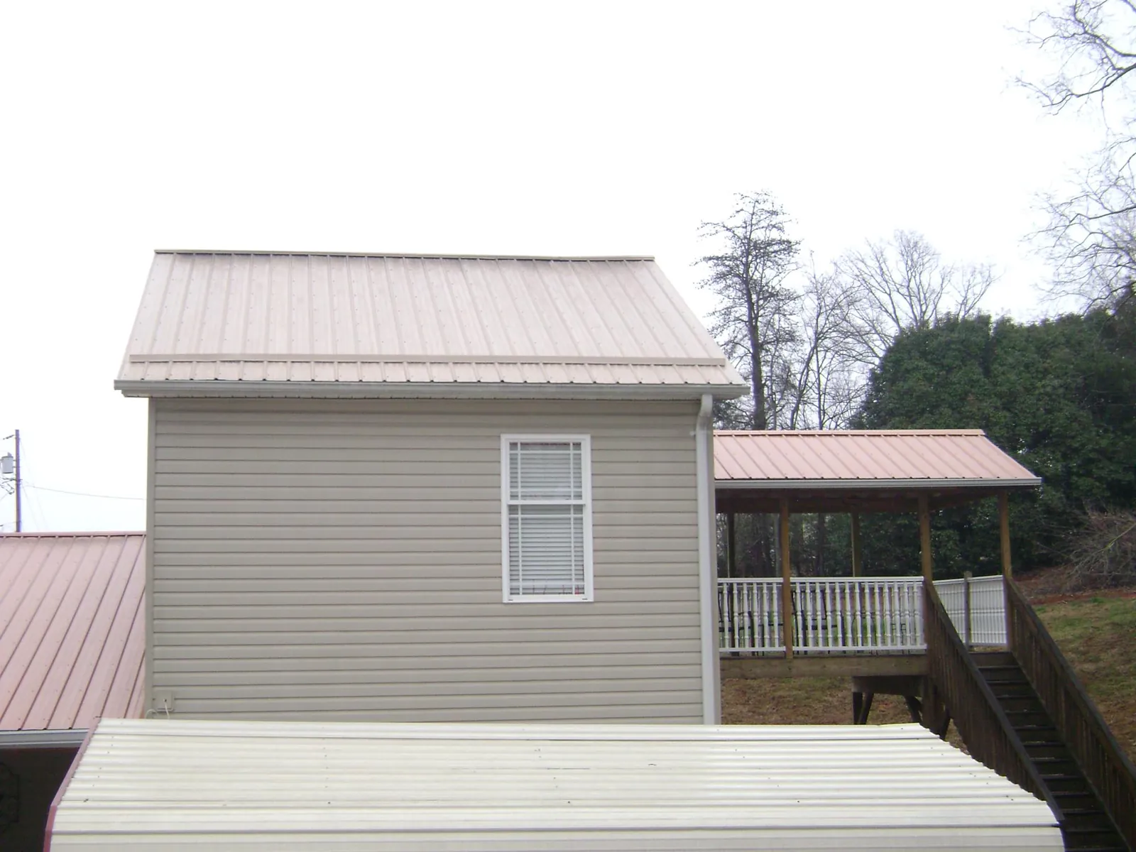 Tan metal roofs on a two story addition and attached porch, from a Roof Replacement job in Duncanville
